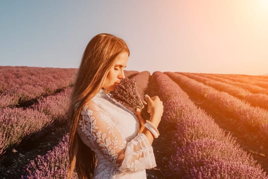 Close up portrait of young beautiful woman in a white dress and a hat is walking in the lavender field and smelling lavender bouquet.