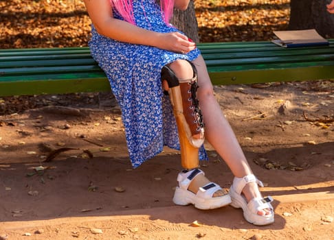 Beautiful young woman leg amputee in a dress sitting on a bench in park at sunny day. Life goes on no matter what.