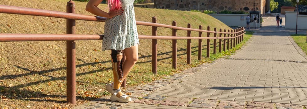 Beautiful young woman leg amputee in a dress walking in park at sunny day. Life goes on no matter what.