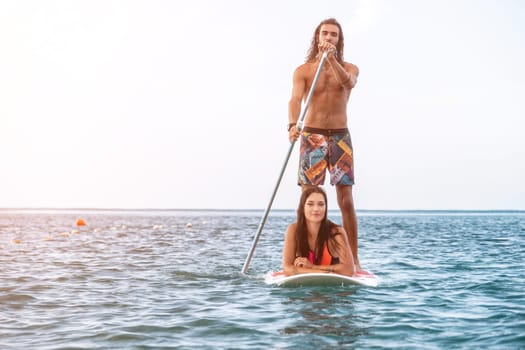 Sea woman and man on sup. Silhouette of happy young woman and man, surfing on SUP board, confident paddling through water surface. Idyllic sunset. Active lifestyle at sea or river