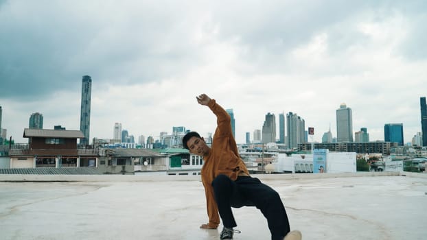 Motion shot of B-boy dance performance by professional street dancer at rooftop with sky scrapper, city view. Attractive asian hipster show energetic footstep. Outdoor sport 2024. Endeavor.