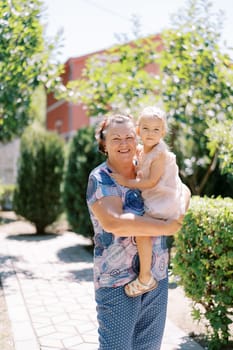 Little girl sitting in the arms of a smiling granny in the garden. High quality photo