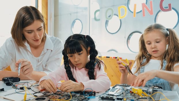 Skilled caucasian teacher teach and explain students about digital electrical tool. Expert girl learn electronic equipment and use to fix motherboard at table with chips and wires placed. Erudition.