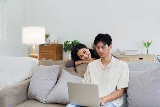 Happy young couple looking laptop relax on sofa in living room watch video on laptop together.