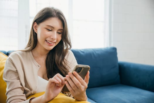 Casually seated on a sofa a smiling woman types on her phone enjoying home relaxation. Engaged in successful communication and technology she radiates contentment. The woman is relaxing.