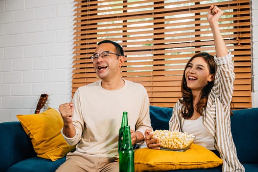 Happy Asian couple boyfriend and girlfriend share the excitement of celebrating a football goal during their leisure weekend at home fostering a perfect sports-loving atmosphere.