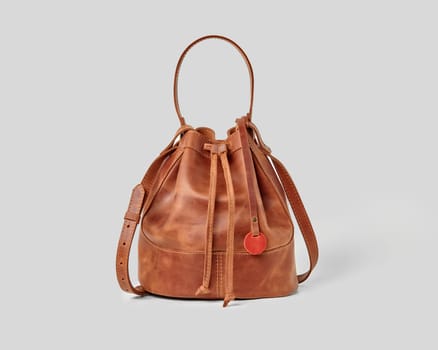 Sophisticated stylish tan leather bucket bag with adjustable drawstrings and shoulder strap, isolated on grey background