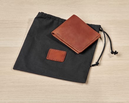 Custom brown leather wallet with initials D.R. embossed, accompanied by black fabric drawstring pouch, presented on light wooden background. Stylish personalized handcrafted accessory