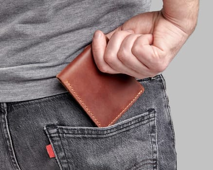 Close-up of man sliding brown leather wallet with embossed initials William into back pocket of grey denim jeans