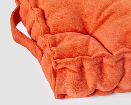 Closeup of puffy bright orange french style seat cushion made of soft velour with handle on white background. Handmade accessory evoking sense of warmth and comfort in home interior design