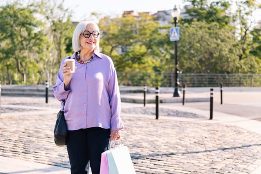 senior woman smiling standing with shopping bags and a takeaway coffee, concept of elderly people leisure and active lifestyle, copy space for text