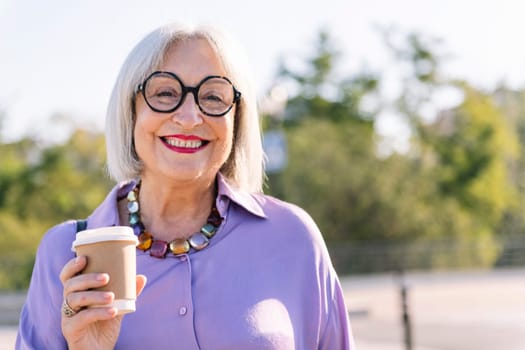 portrait of a smiling senior woman looking at camera with a takeaway coffee, concept of elderly people leisure and active lifestyle, copy space for text