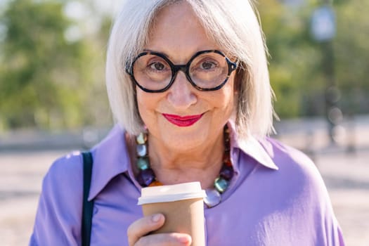 close up portrait of a smiling senior woman looking at camera with a takeaway coffee, concept of elderly people leisure and active lifestyle