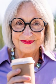 close up portrait of a smiling senior woman looking at camera with a takeaway coffee, concept of elderly people leisure and active lifestyle, copy space for text