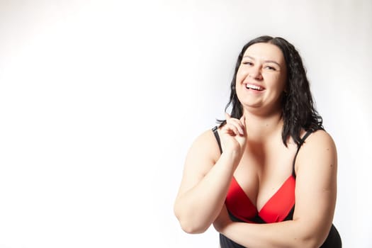Portrait of attractive dreamy thick woman in red black swimsuit posing on white background. Body positive, photoshoot, selfie. Funny plus size model