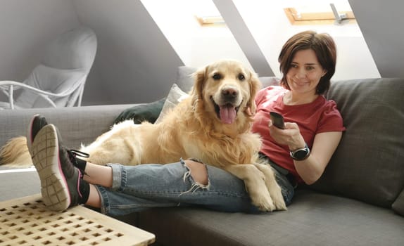 Pretty girl with golden retriever dog sitting on sofa and petting doggy. Young woman with purebred pet labrador in loft room