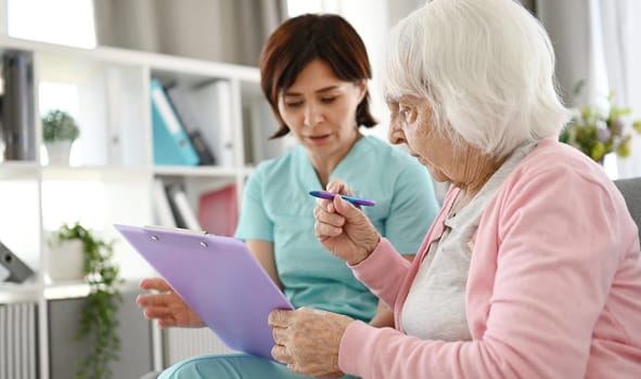 Nurse Helping For Elderly Woman For Sign Documents At Nursing Home