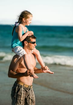 Father holding daughter on shoulders at sea coast and looking into the distance. Family dad and little pretty child kid at beach at summer