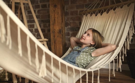 Preteen child girl lying in hammock in loft room at home. Pretty female kid enjoying summer vacation