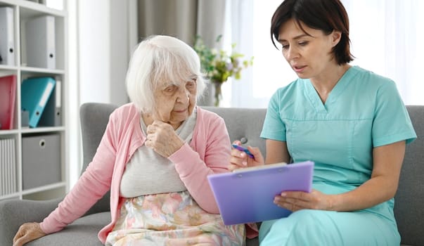 Doctor Reads Elderly Woman Health Documents In Bright Hallway