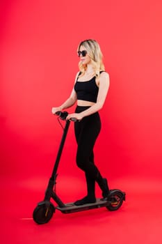 A blonde woman on a red background sitting on electro scooter and resting, copy space