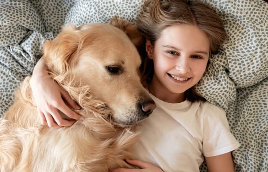 Happy Little Girl Hugging Golden Retriever Dog And Smiling Lying On A Bed