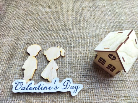 Wooden figurines of a couple, a house and the inscription Valentine's Day. The concept of a holiday of love and lovers. Background, texture, place for text and copy space