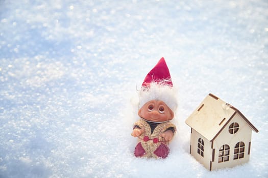Cute little funny dwarf and small wooden house in snow in winter landscape. Wizard on snowy background. Christmas and New Year