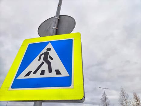 A pedestrian crossing sign on the background of a gray sky with clouds. Drawing, pictogram for pedestrians crossing the road