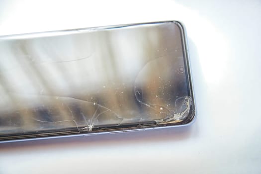 Close-Up View of a Cracked Smartphone Screen Against White Background. the detailed texture of a shattered smartphone screen, emphasizing extensive damage to the device