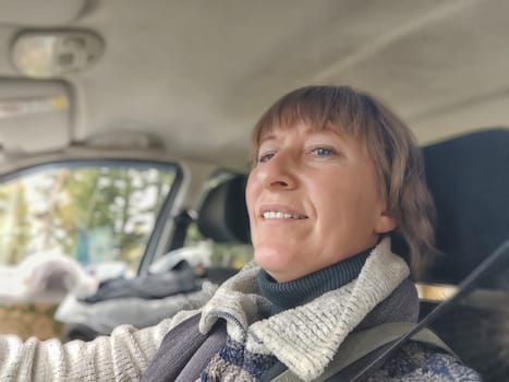 Funny cute blonde girl or a middle-aged woman driving a car in summer, autumn, spring day. A female driver on a solo trip