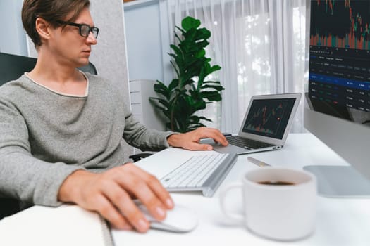 Business trader using computer and laptop to search highest profit value of dynamic increased stock market graph on working desk, analyzing exchange rate value on screen at modern office. Pecuniary.