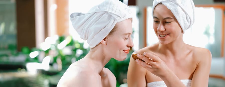 Couple of beautiful woman interested in homemade facial masks while sitting at spa salon. Attractive woman in white towel enjoy herbal masks with her friend surrounded by nature. Tranquility.