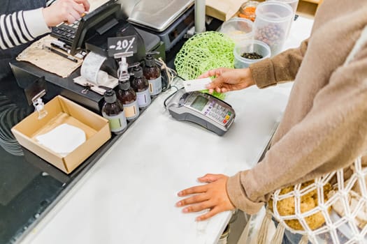 Woman paying with contactless credit card with NFC technology in local zero waste grocery store at cash desk