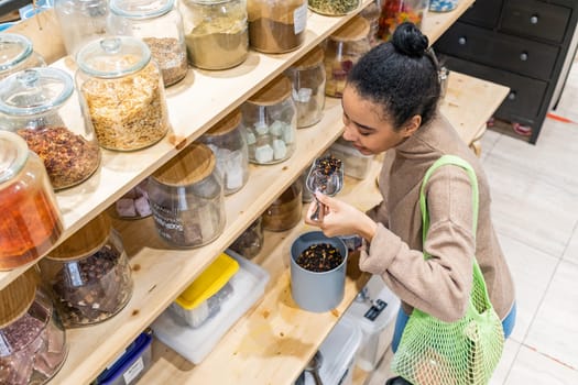 African American woman buying organic tea in local zero waste grocery store. Woman smells organic tea in sustainable grocery store.