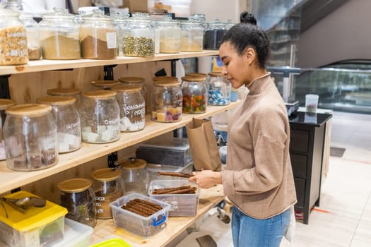 African American woman buying sugar-free fruit roll healthy dessert made of dried fruits in local zero waste grocery store. Woman buying organic vegan food in sustainable grocery store.