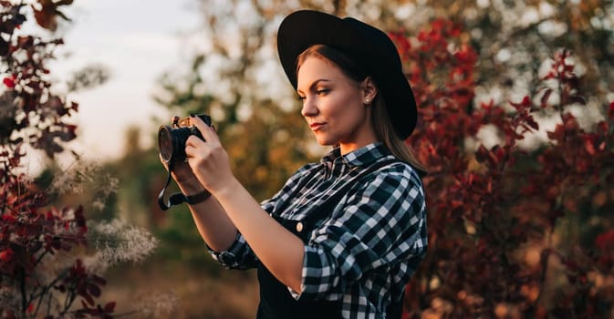 Young pretty woman takes pictures with DSLR camera outdoors on autumn background. Analog digital photocamera. High quality photo