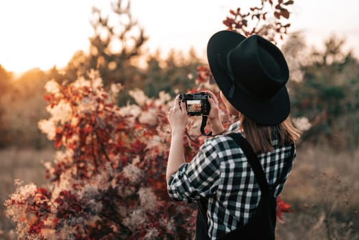 Young pretty woman takes pictures with DSLR camera outdoors on autumn background. Analog digital photocamera. High quality photo