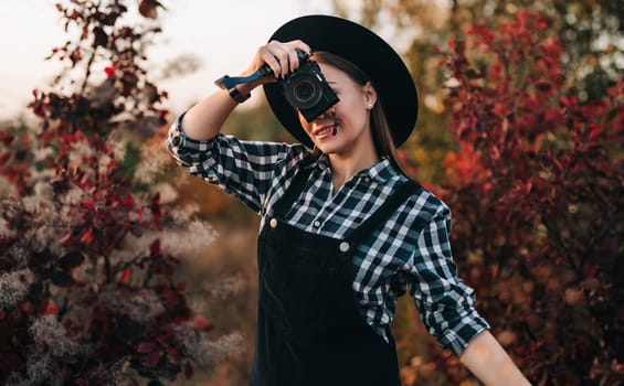 Young pretty woman takes pictures with DSLR camera outdoors on autumn background. Analog digital photocamera. High quality photo