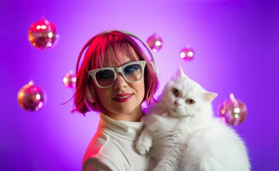 Disco woman with cat in fashion glasses listening music, dancing with headphones in colorful studio. Party, radio, headset concept.