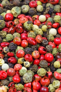 Background image. Top view of a mix of red, green, black, gray and white peppercorns. Vertical frame.