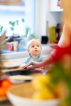 Mother and little toddler baby boy making pancakes for breakfast together in domestic kitchen. Family, lifestyle, domestic life, food, healthy eating and people concept