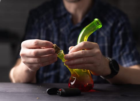 Man Fills Bong With Cannabis Leaves, Hands In Close-Up View
