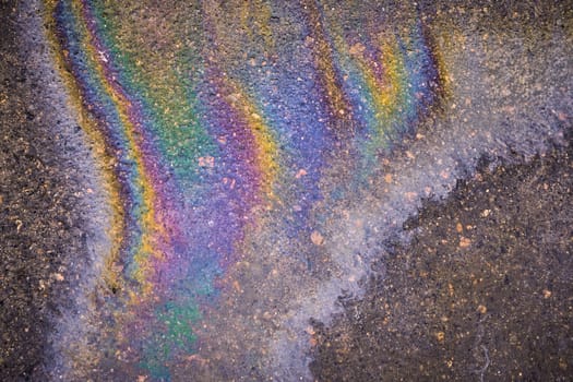 rainbow stripes on wet asphalt after fuel spill from car