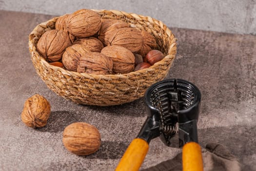 Basket with walnuts and hazelnuts and a nut cracker on a rustic kitchen counter.