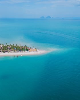 Koh Muk a tropical island with palm trees and soft white sand, and a turqouse colored ocean, drone top view at a sandbank in a blue turqouse colored ocean in Koh Mook Trang Thailand