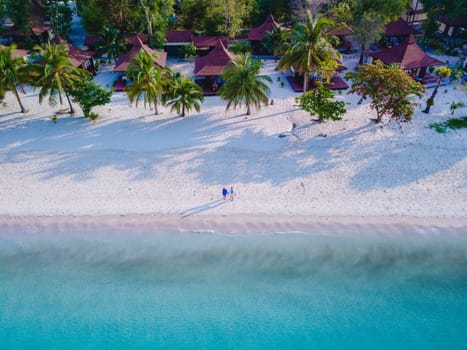Drone view at a couple walking on the white sandy tropical beach of Koh Muk with palm trees soft white sand, and a turqouse colored ocean in Koh Mook Trang Thailand at summer