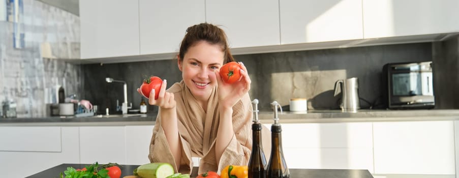 Portrait of beautiful woman cooking in the kitchen, chopping vegetables on board, holding tomatoes, lead healthy lifestyle with preparing fresh salads, vegan meals.