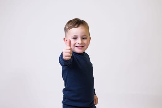 portrait of cute boy in casual clothes showig thumbs up sign on white background