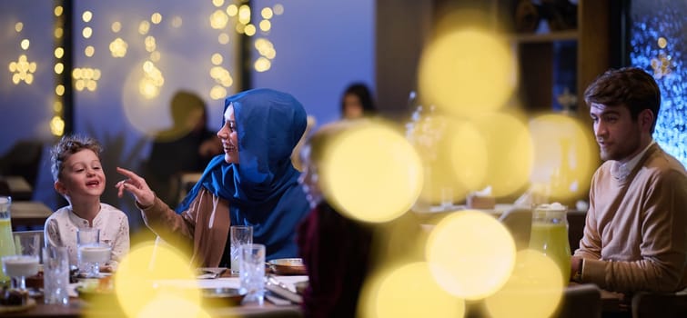 In a modern restaurant, an Islamic couple and their children joyfully await their iftar meal during the holy month of Ramadan, embodying familial harmony and cultural celebration amidst the contemporary dining ambiance.